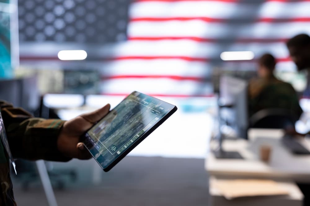 National security professionals monitor cybersecurity networks on a table with a large American flag blurred in the background